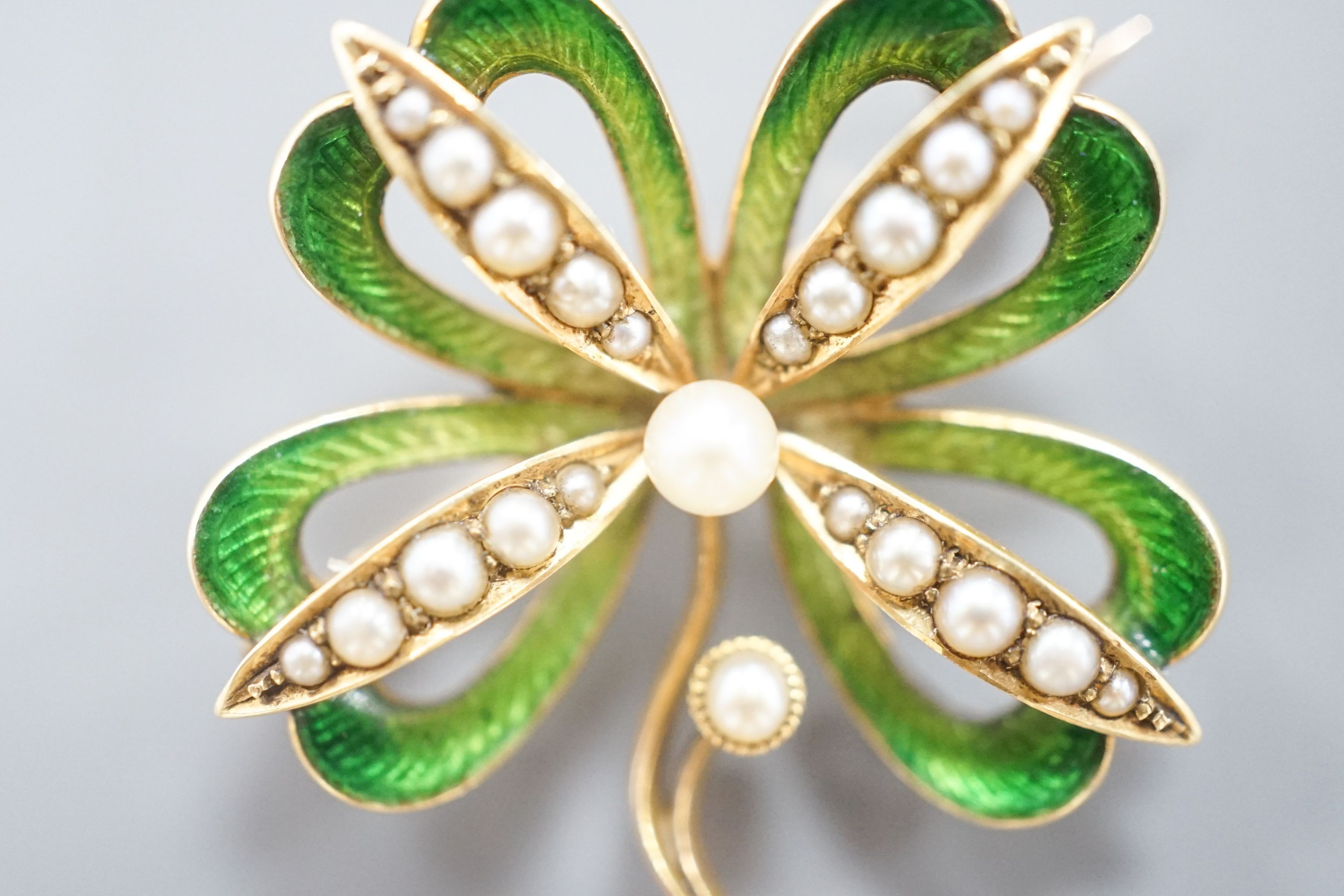 An Edwardian 15ct, seed pearl and green enamel set clover brooch, with later bale attachment, width 24mm, gross weight 4.4 grams.